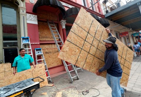 Cesar Reyes, right, carries a sheet of plywood as he helps install window coverings at a business in Galveston.