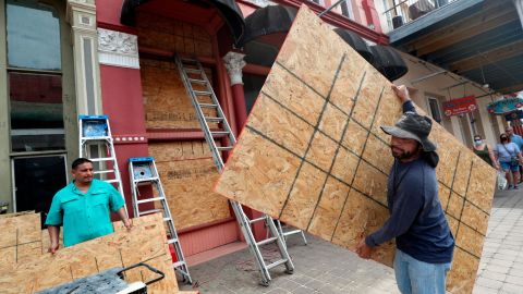 Cesar Reyes, right, carries a sheet of plywood to cut to size as he and Robert Aparicio, left, and Manuel Sepulveda, not pictured, install window coverings in Galveston on Monday.
