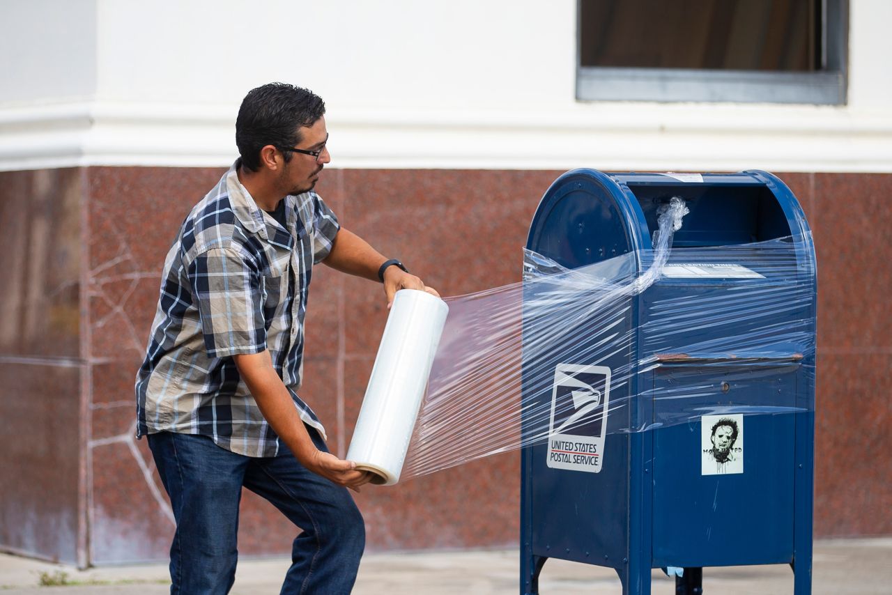 A US Postal Service employee covers a mailbox with plastic wrap in Galveston, Texas. The plastic wrap signals that the final mail has been cleared from the box, and it prevents people from placing mail inside that could be lost in a flood.