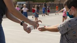 A teacher sprays hand sanitizer on a student's hands following recess at an elementary school in Surprise, Arizona, U.S., on Thursday, Aug. 20, 2020. Arizona's downward trend of coronavirus cases means parts of the state could meet all three metrics the state's health and education departments set for at least a partial reopening of schools by Labor Day. Schools are not bound by the rules, and some have reopened already, the Associated Press reports. 
