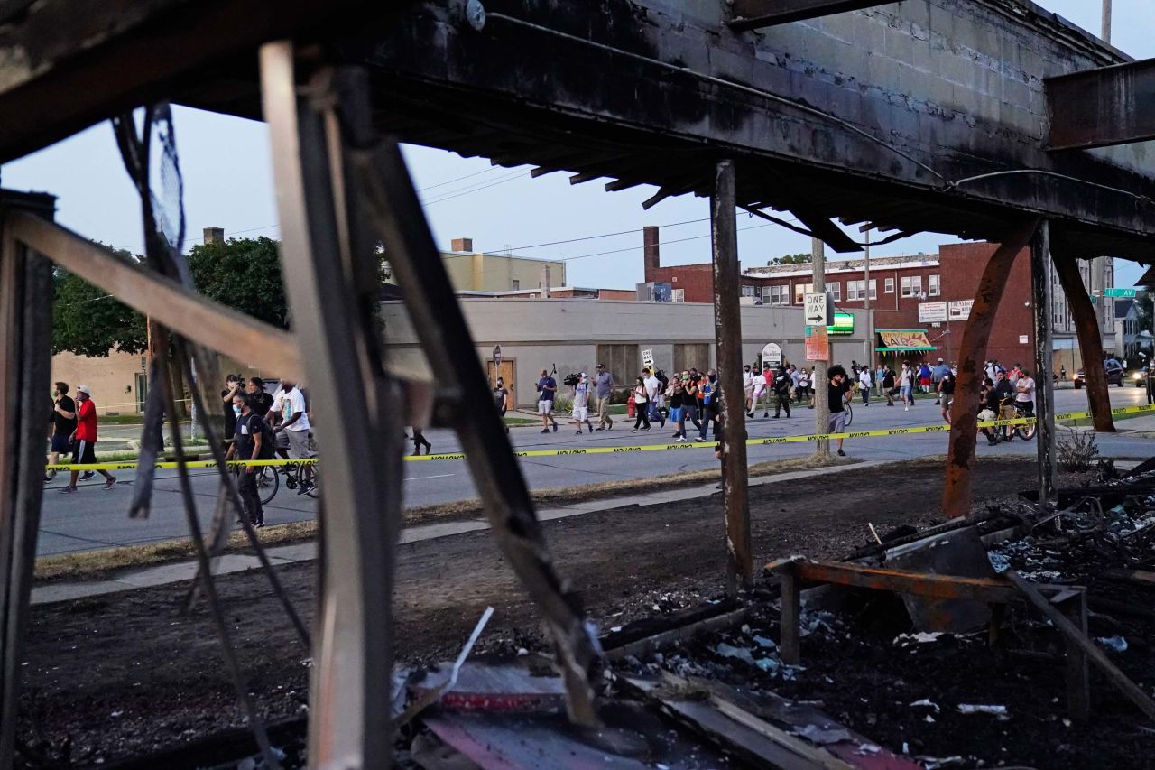 Protesters march past a burned-out building that was damaged during protests.
