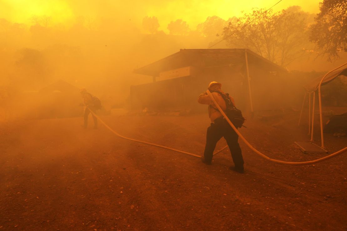Firefighters carry a hose towards a burning structure as the LNU Lightning Complex Fire burns near Napa, California. This year, fewer inmates are able to help to fight the wildfires.