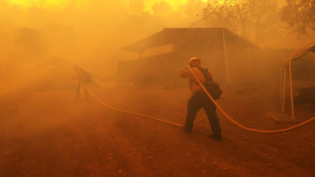Firefighters carry a hose towards a burning structure as the LNU Lightning Complex Fire burns near Napa, California. This year, fewer inmates are able to help to fight the wildfires.