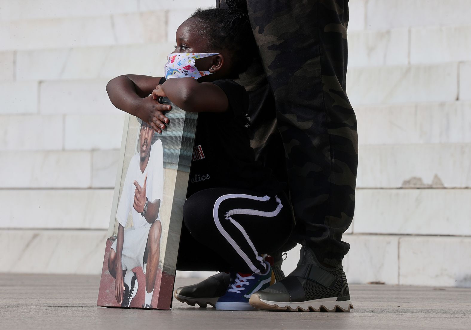 The 4-year-old daughter of Marqueese Alston, who was shot and killed by Washington's Metropolitan Police on June 12, 2018, holds a photograph of her father as demonstrators gather at the Lincoln Memorial.