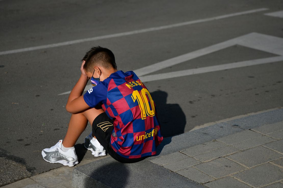 A disappointed young Barcelona supporter sporting Lionel Messi's jersey sits on the pavement outside the Barcelona training ground hoping for a glimpse of his hero.