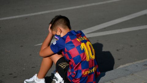 A disappointed young Barcelona supporter sporting Lionel Messi's jersey sits on the pavement outside the Barcelona training ground hoping for a glimpse of his hero.