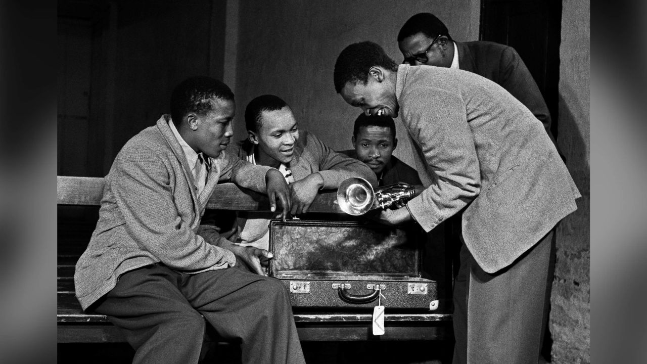 A young Hugh Masekela receives the trumpet from jazz legend Louis Armstrong.