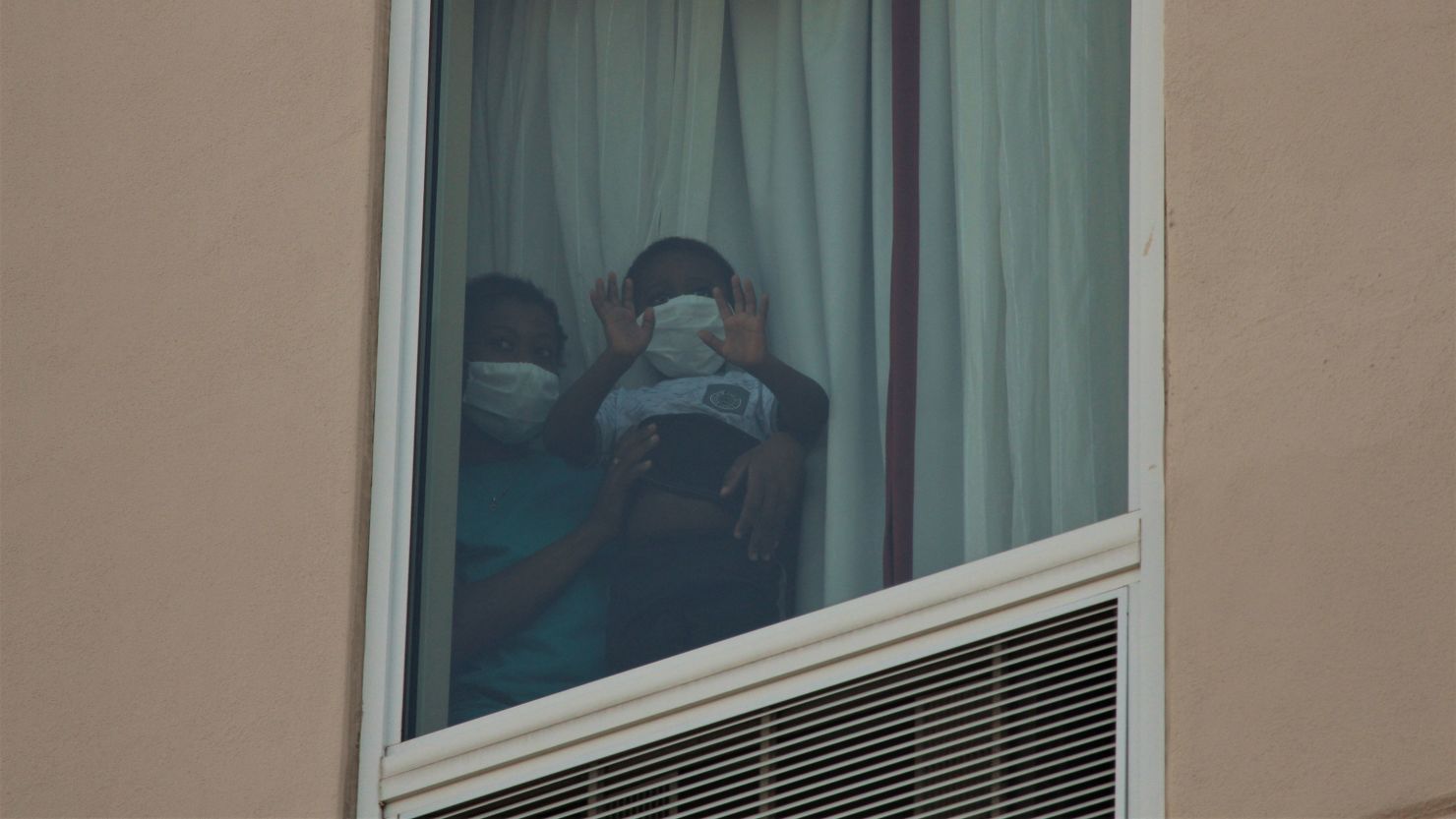 Migrants peak out of the window of the fourth floor of a Hampton Inn in McAllen, Texas, on Thursday July 23, 2020.