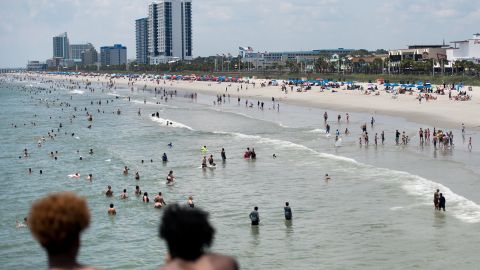 Two young men watch as people wade in the ocean on July 4, 2020, in Myrtle Beach, South Carolina. Vacationers traveled to the SC beach despite growing concerns about the the spread of the coronavirus.