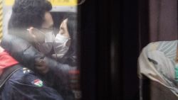 TOPSHOT - A couple wearing face masks kiss on an underground metro train as another passenger (R) is reflected on a platform glass door during a Lunar New Year of the Rat public holiday in Hong Kong on January 27, 2020, as a preventative measure following a coronavirus outbreak which began in the Chinese city of Wuhan. (Photo by Anthony WALLACE / AFP) (Photo by ANTHONY WALLACE/AFP via Getty Images)