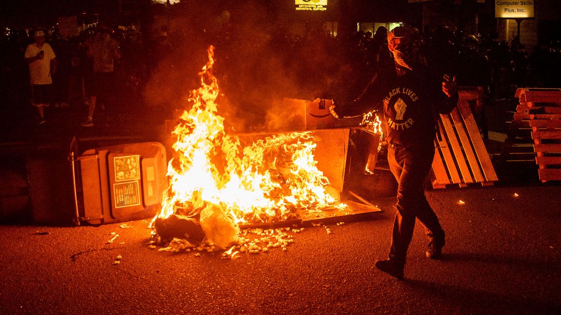 A protester passes a dumpster fire in Portland, Oregon, on Saturday, September 5. Saturday marked the 100th night of protests in the city since the death of George Floyd in late May.