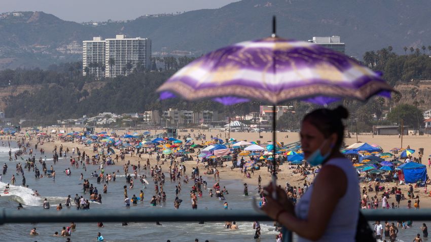 A woman uses an umbrella to protect herself from the sun at Santa Monica pier while people enjoy the beach on the second day of the Labor Day weekend amid a heatwave in Santa Monica, Caifornia on September 6, 2020.