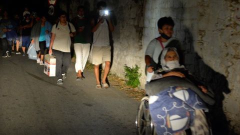 Refugees and migrants leave as a fire burns at the Moria refugee camp.