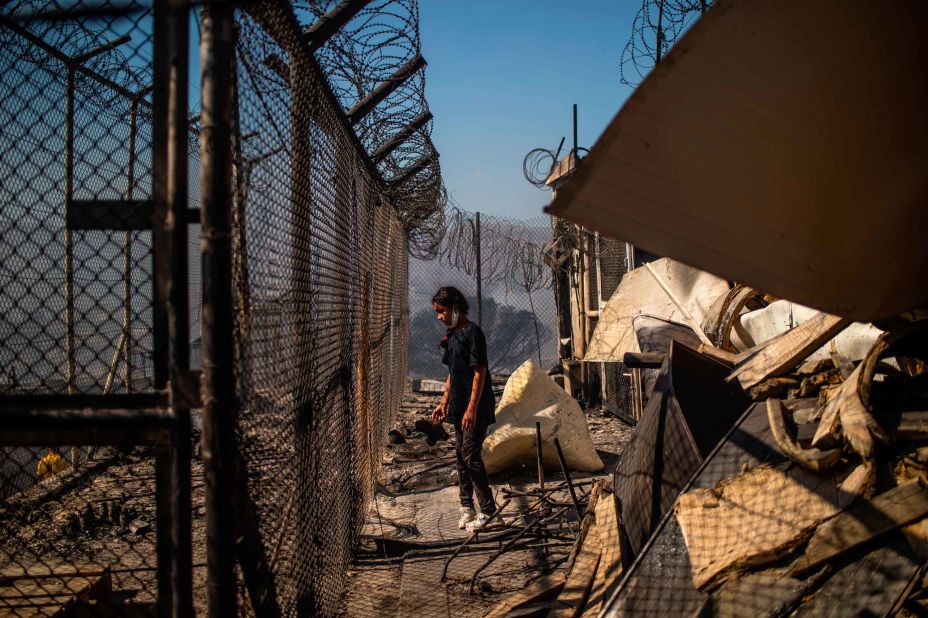 A girl stands amid burnt wreckage.