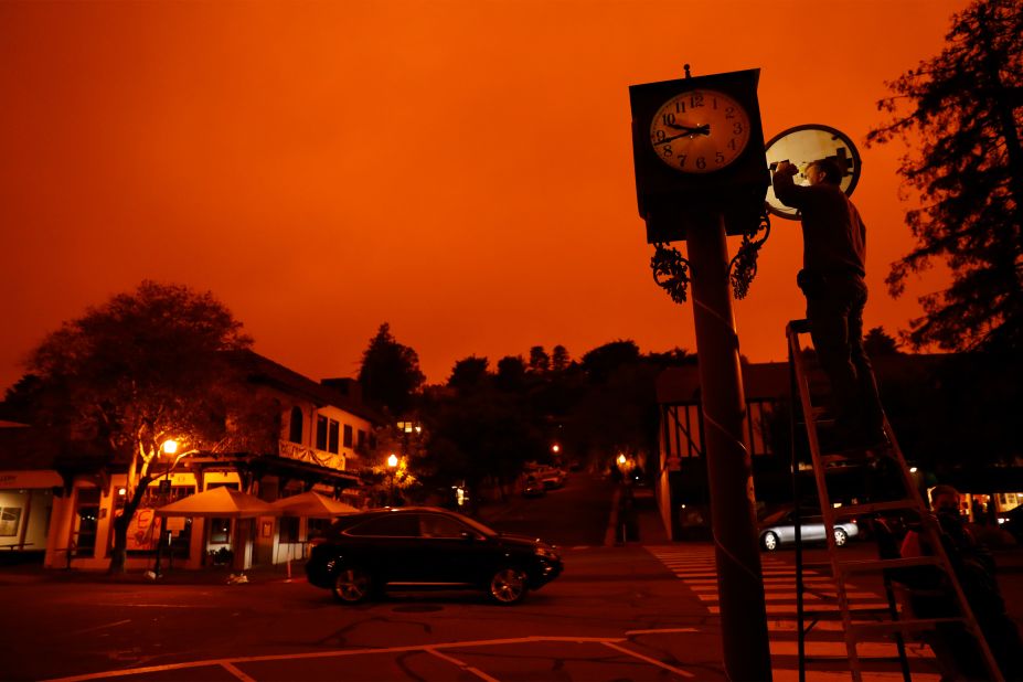 Bejhan Razi, a senior building inspector in Mill Valley, California, checks out repairs on a lamp-post clock as the sky is illuminated by nearby wildfires.