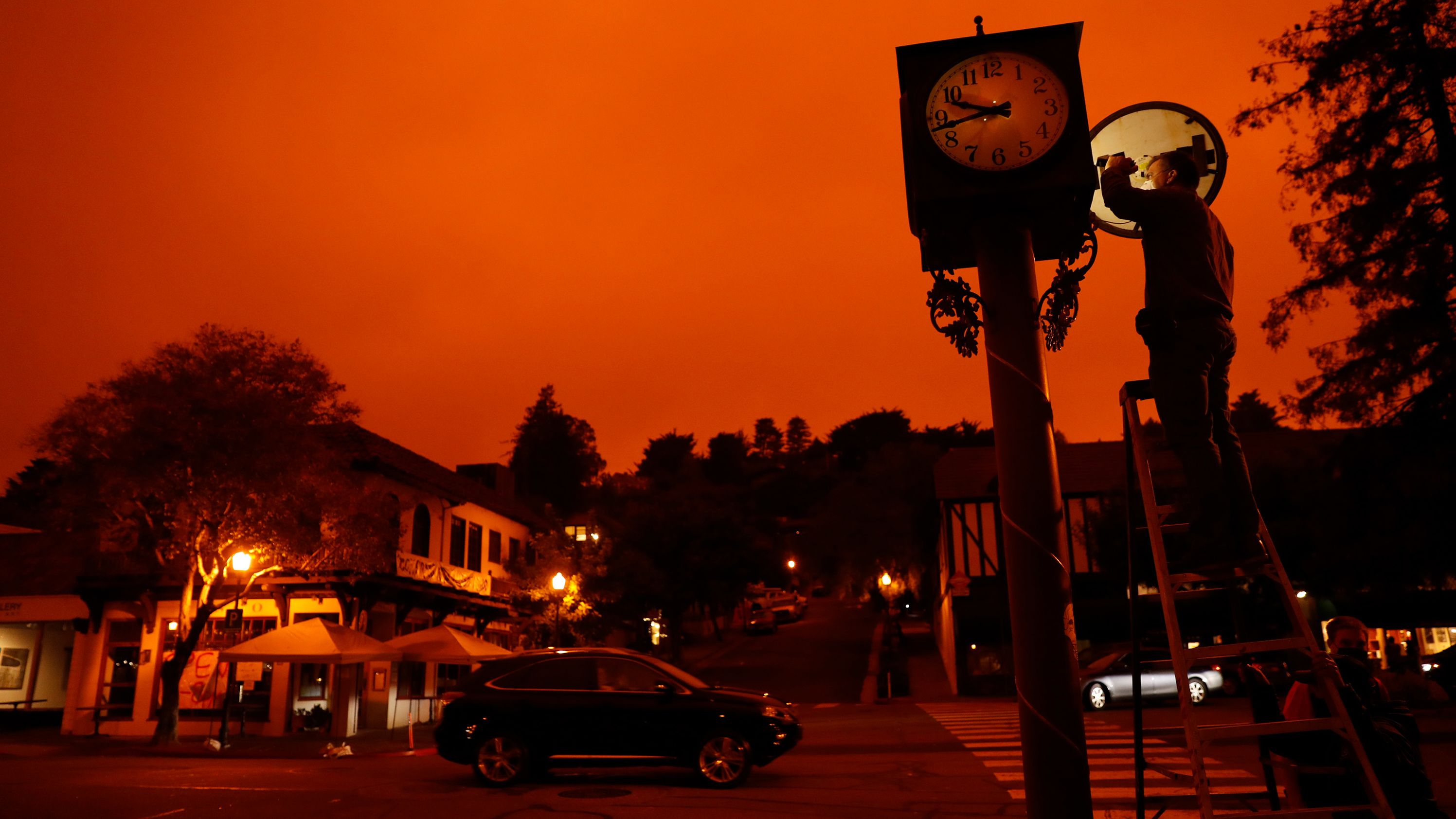 Bejhan Razi, a senior building inspector in Mill Valley, California, checks out repairs on a lamp-post clock as the sky is illuminated by nearby wildfires.