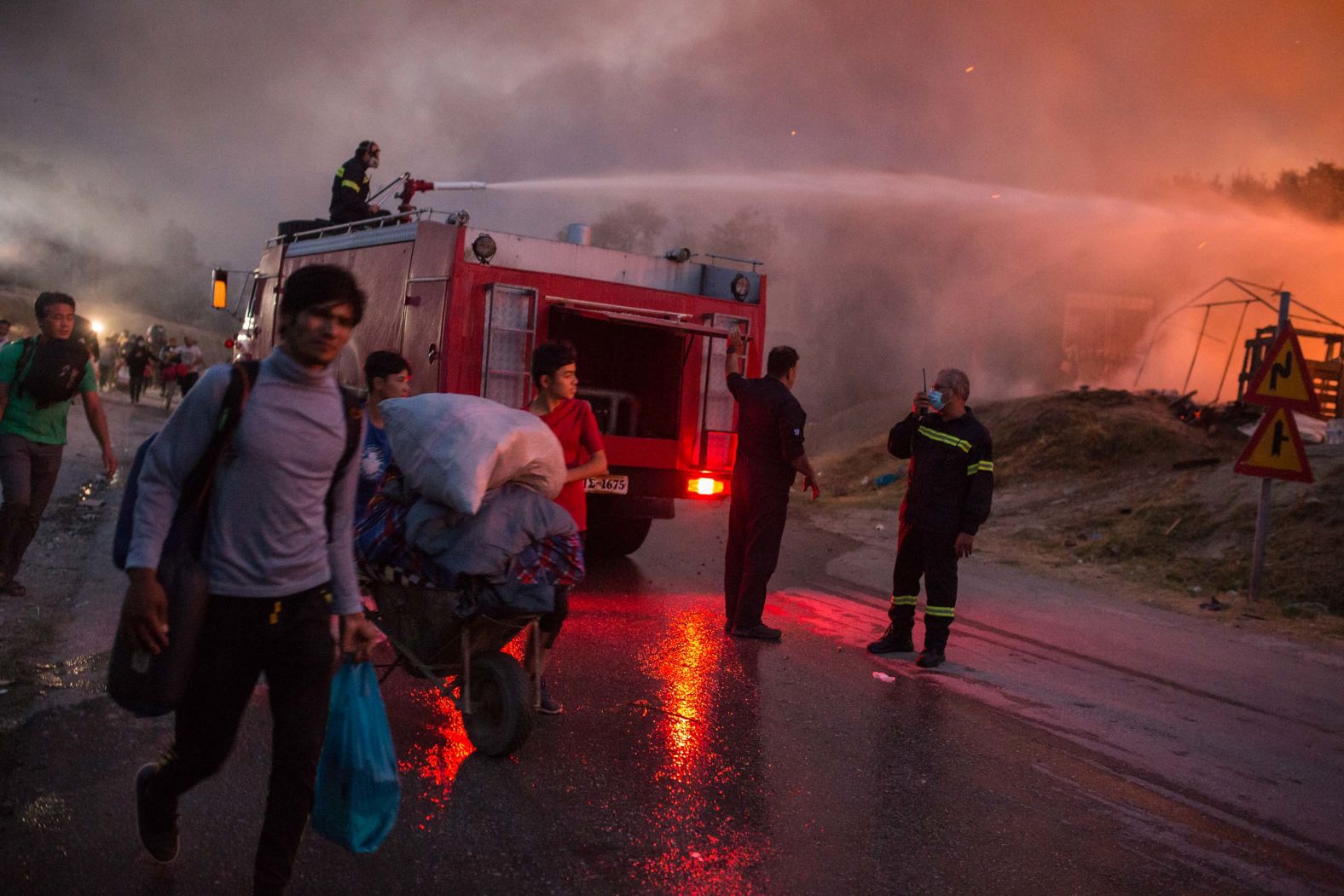 People evacuate the camp with their belongings as firefighters work to extinguish the blaze.