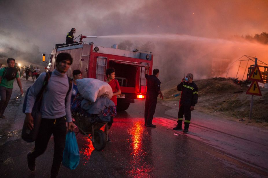 People evacuate the camp with their belongings as firefighters work to extinguish the blaze.