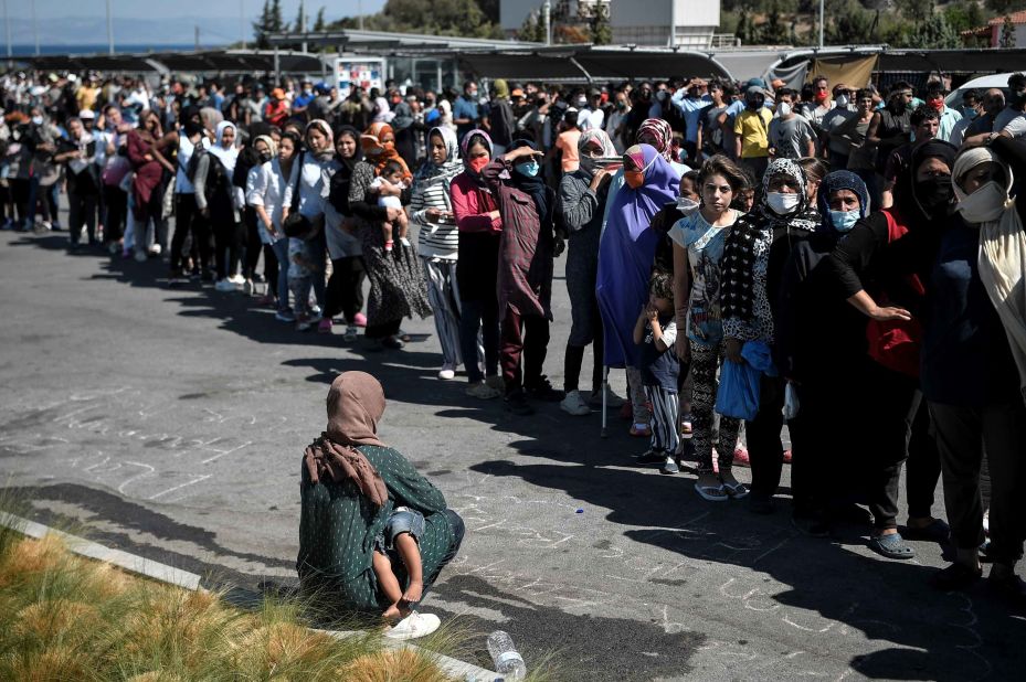 Migrants line up for water and food distribution at a supermarket parking lot where many have taken refuge.
