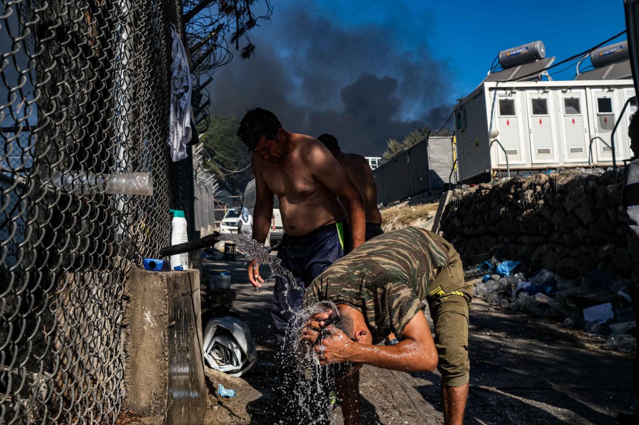 Asylum seekers bathe in the smoldering camp.