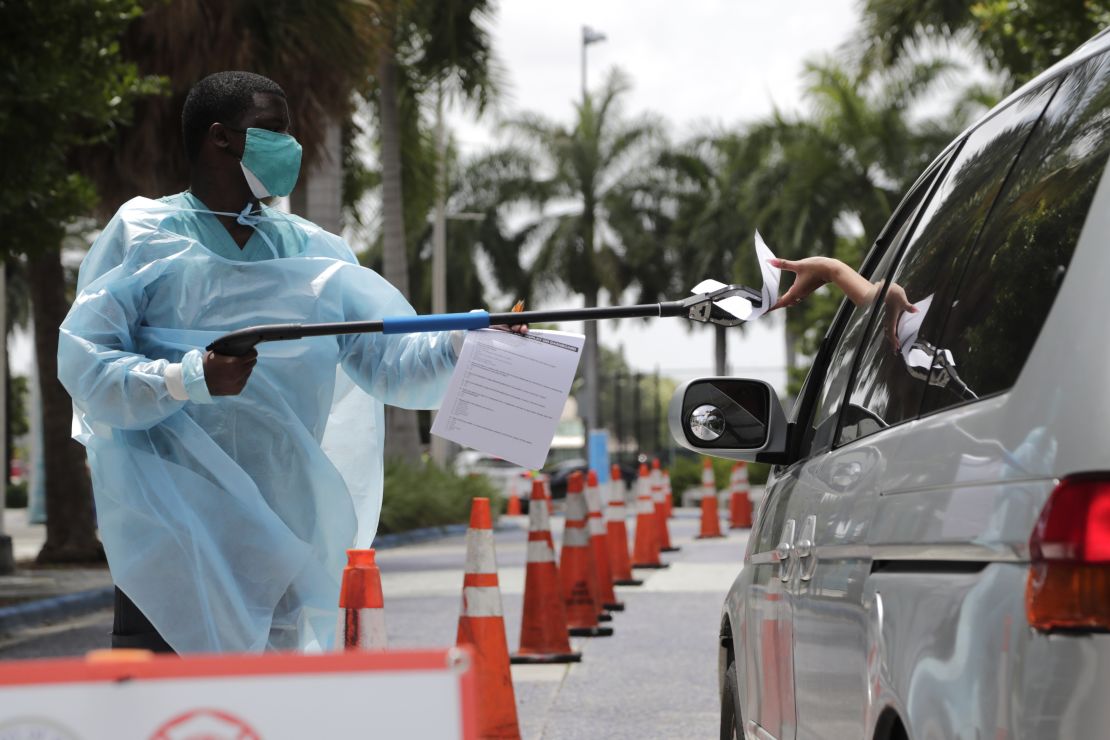 Healthcare worker Dante Hills passes paperwork to a woman in a vehicle at a COVID-19 testing site in Miami. 