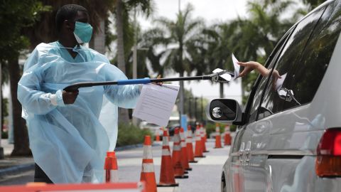 Healthcare worker Dante Hills passes paperwork to a woman in a vehicle at a COVID-19 testing site in Miami.