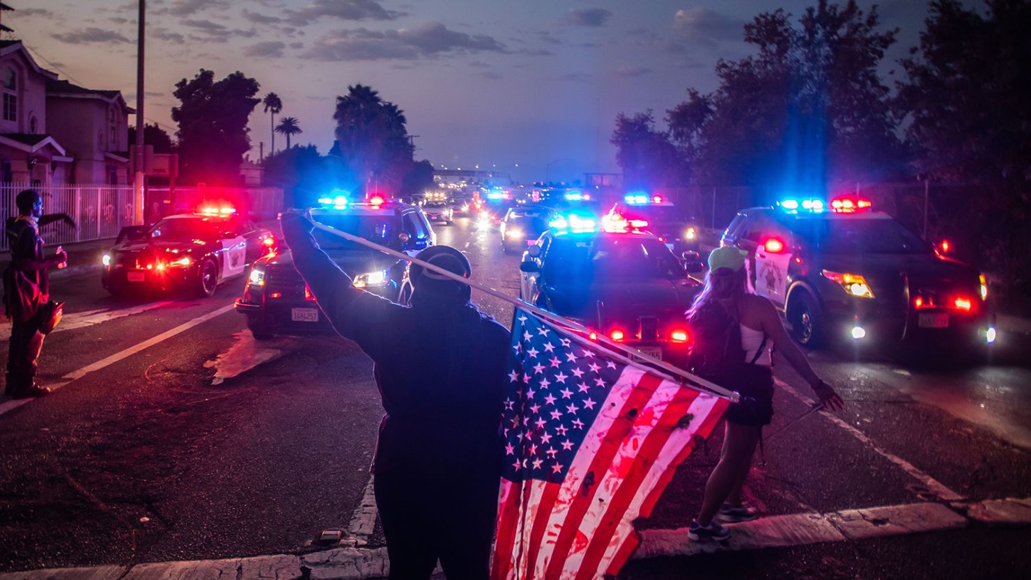A man holds a US National flag in front of Police cars during a demonstration  in Los Angeles, California on September 5, 2020.