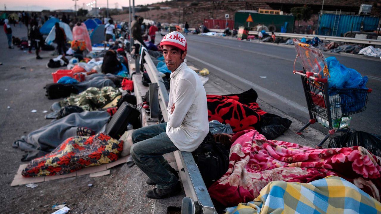A man sits on a crash barrier as homeless migrants and refugees sleep on a roadside following the blaze.