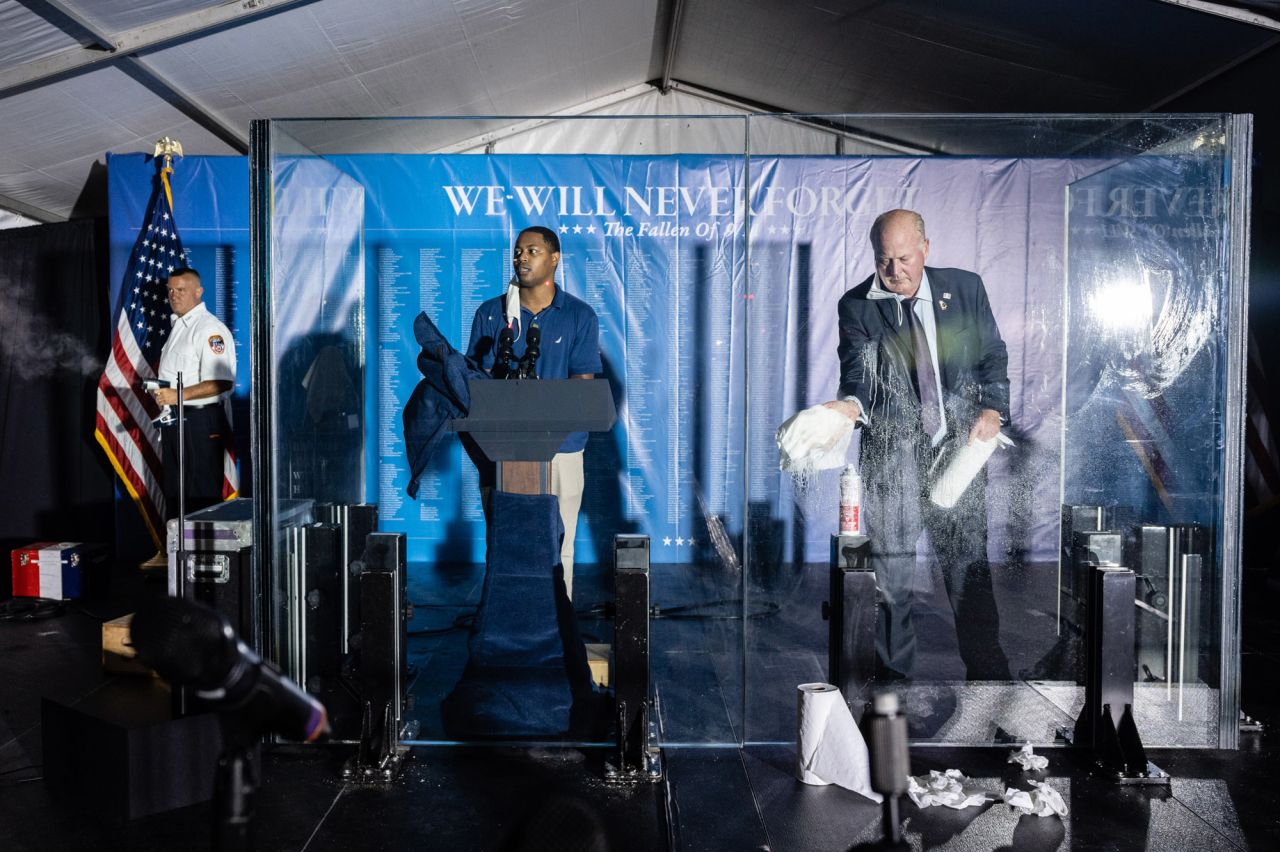 Preparations are made before that start of the Tunnel to Towers ceremony. At left, a firefighter steam-presses a flag. At center, a man tests the sound system while another man next to him cleans the glass where the vice president and his wife would speak.