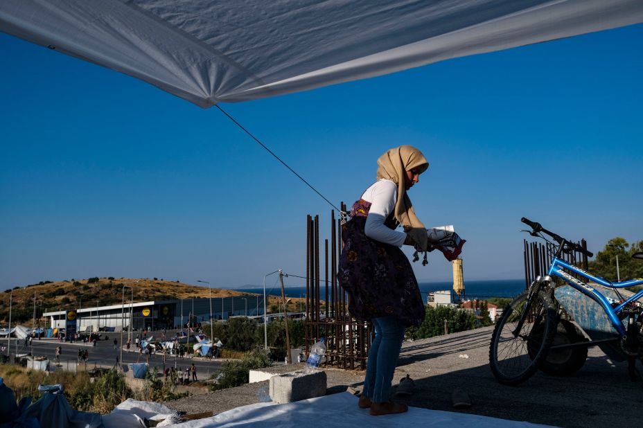A displaced Syrian migrant cleans up around her new tent, located on the roof of an industrial site. The supermarket in the background is where many Greeks and migrants have shopped, photographer Byron Smith said.