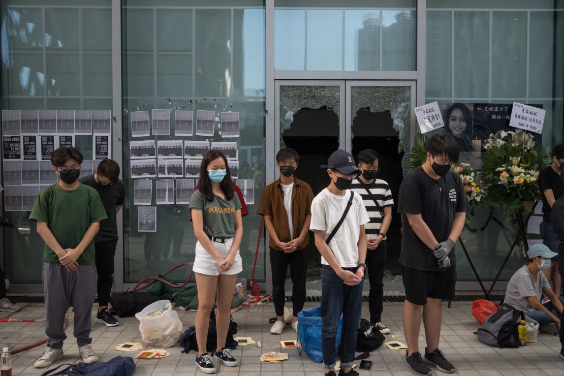 People stand in silent tribute at the Hong Kong Design Institute. Behind them, broken windows can be seen, the result of protests over an alleged lack of transparency regarding Chan's last movements. 