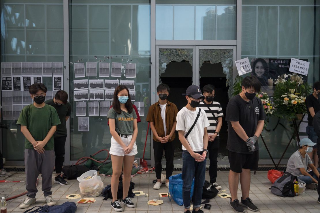 People stand in silent tribute at the Hong Kong Design Institute. Behind them, broken windows can be seen, the result of protests over an alleged lack of transparency regarding Chan's last movements.
