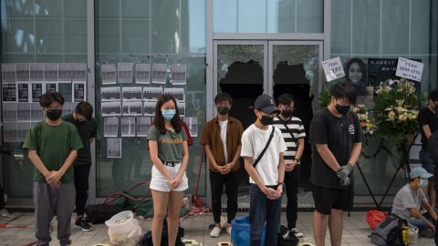 People stand in silent tribute at the Hong Kong Design Institute. Behind them, broken windows can be seen, the result of protests over an alleged lack of transparency regarding Chan's last movements. 
