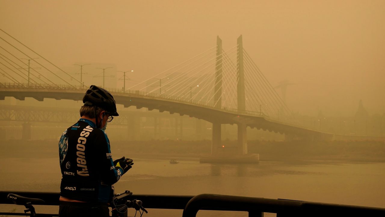 A man stops on his bike along the Willamette River as smoke partially obscures the Tilikum Crossing Bridge on Saturday in Portland, Oregon.