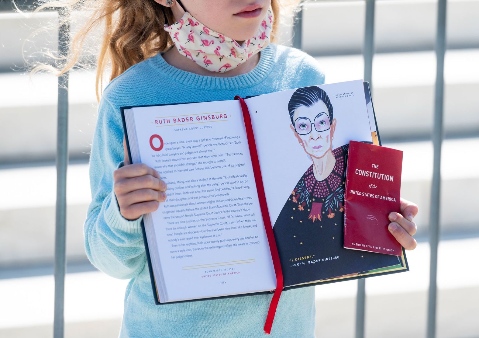 A girl near the Supreme Court holds up a book page about Ginsburg and a copy of the US Constitution on September 19.