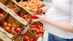 Pregnant woman in a food store or a supermarket choosing fresh organic tomatoes. Healthy eating for expectant mother