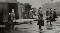 The St Louis Red Cross Motor Corps on duty with mask-wearing women holding stretchers at the backs of ambulances during the Influenza epidemic, St Louis, Missouri, October 1918. 
