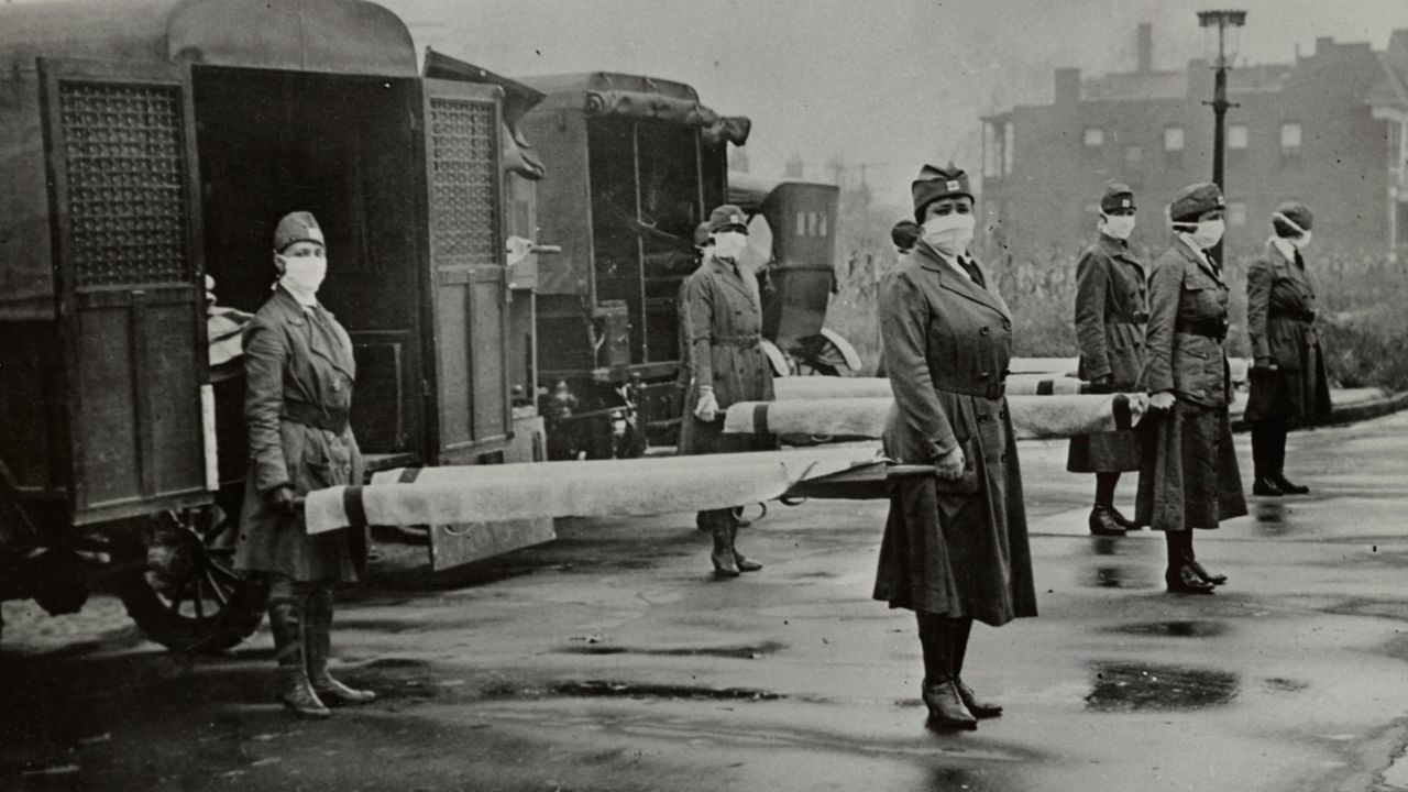 The St. Louis Red Cross Motor Corps was on duty with mask-wearing women holding stretchers at the backs of ambulances during the influenza epidemic in Missouri in October 1918. 