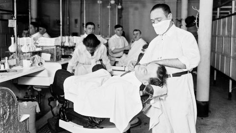 A man receives a shave from a barber in an influenza mask during the ongoing pandemic in Chicago in 1918.