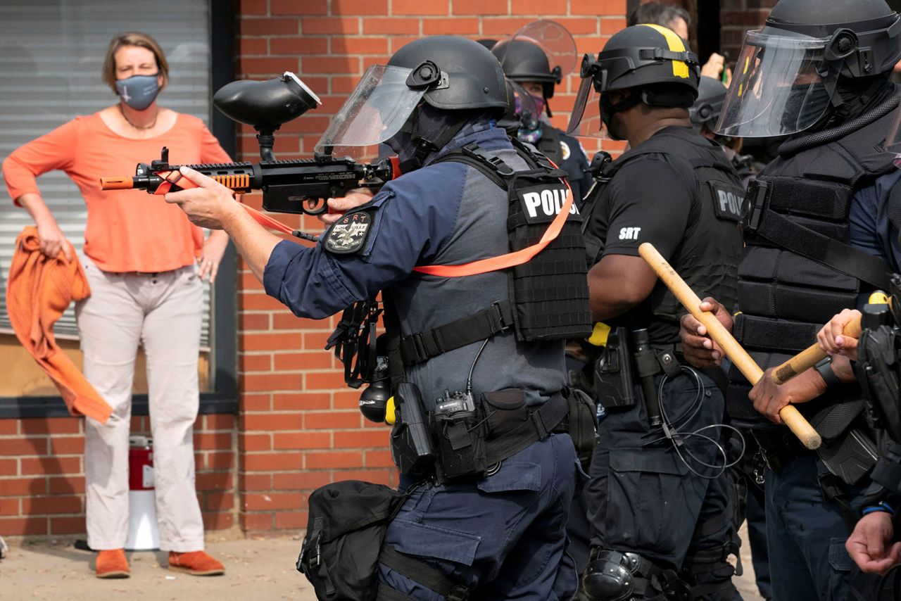 A Louisville police officer fires a pepper ball gun into a crowd of protesters.