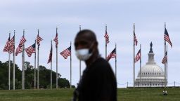 A pedestrian wears a mask while walking across the street from the World War II Memorial as people gathered at area war memorials in commemoration of Memorial Day on Monday May 25, 2020 in Washington, DC. Many of the area Memorial Day events were canceled due to the coronavirus. (Photo by Matt McClain/The Washington Post via Getty Images)