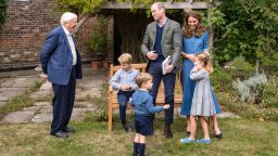 In this Thursday, Sept. 24, 2020 photo released by Kensington Palace, Britain's Prince William, centre, and Kate, the  Duchess of Cambridge, react with Naturalist David Attenborough, left, with their children, Prince George, seated, Princess Charlotte, right and Prince Louis, foreground, in the gardens of Kensington Palace in London after Prince William joined Attenborough to watch a private outdoor screening of his upcoming film - David Attenborough: A Life On Our Planet. (Kensington Palace via AP)