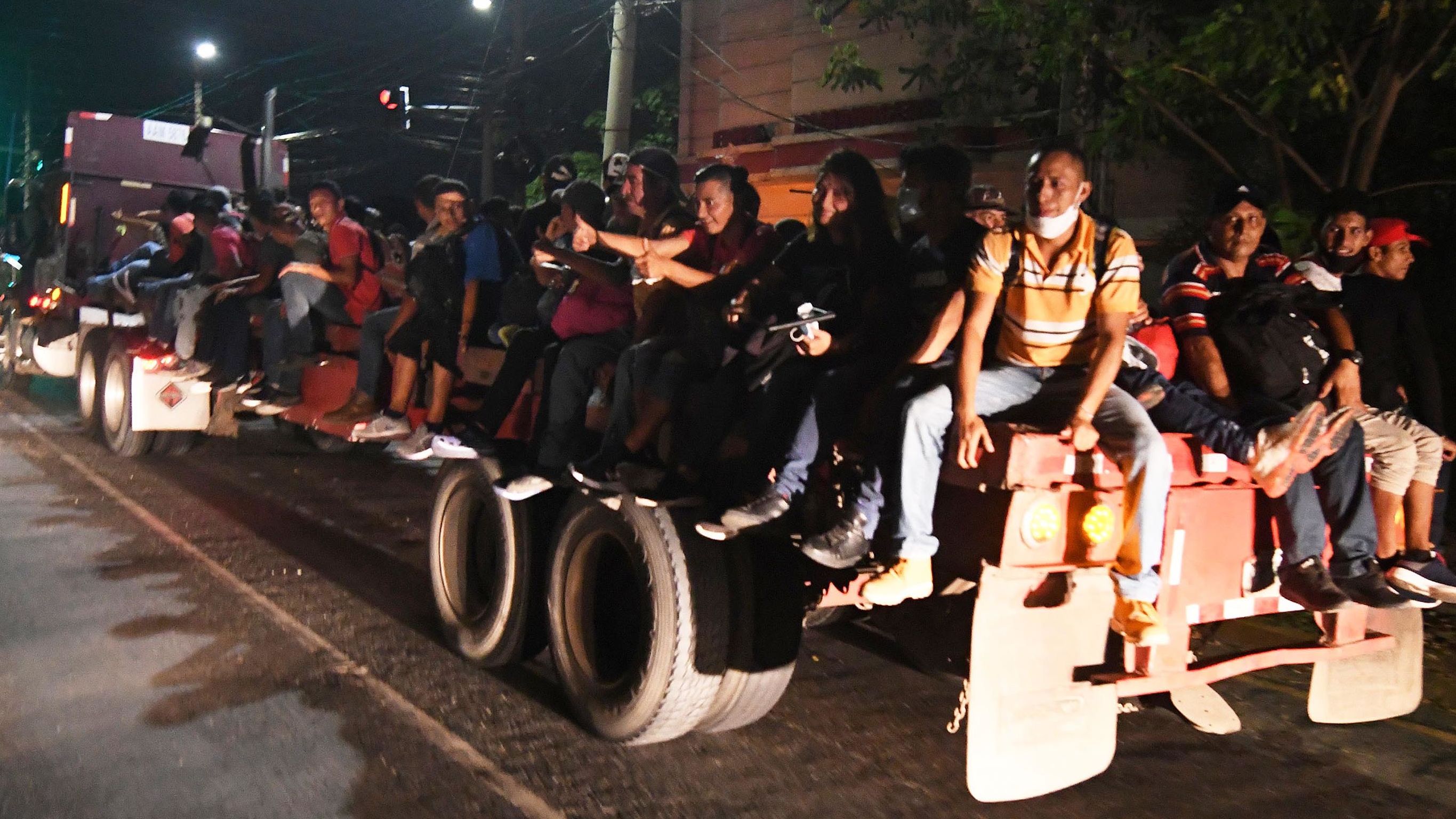 Hondurans sit on the flat bed of a truck as they leave for the US.