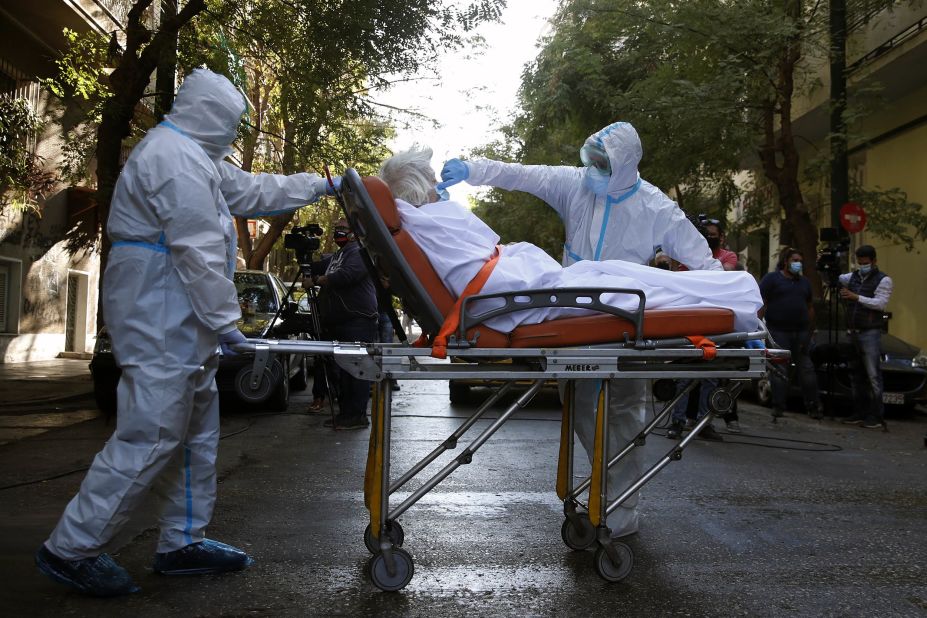 A paramedic adjusts a patient's face mask outside an Athens, Greece, nursing home where dozens of people tested positive for Covid-19.