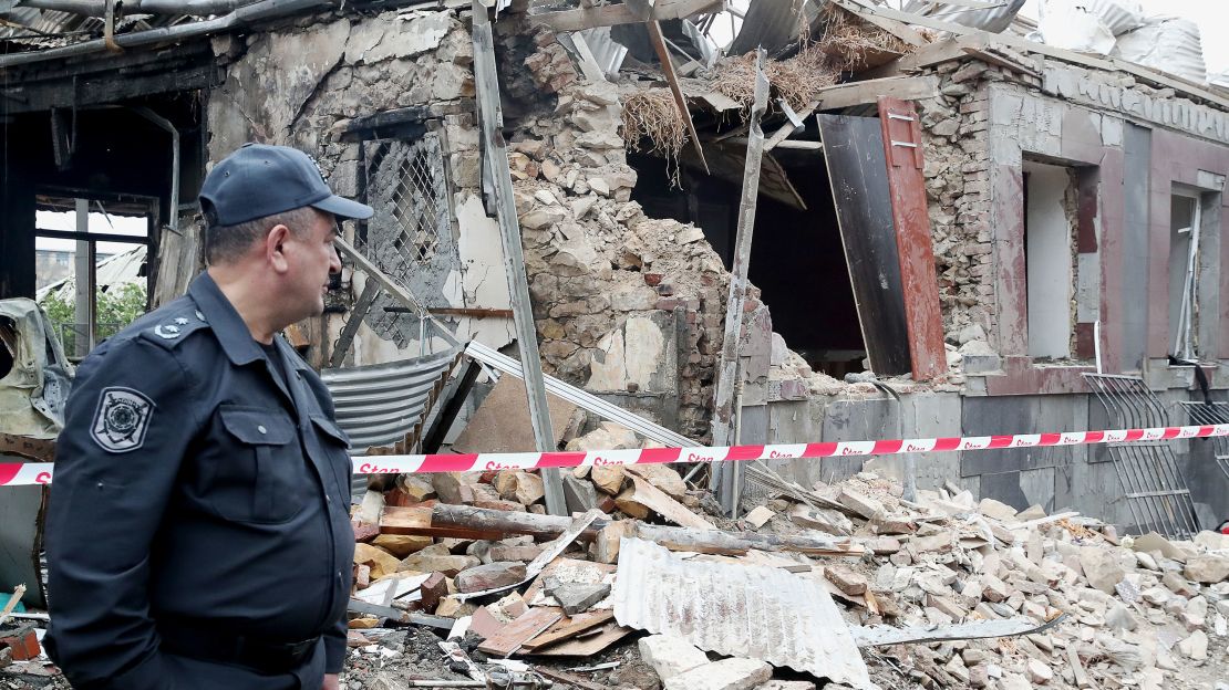 A policeman stands in front of a building damaged by shellfire.