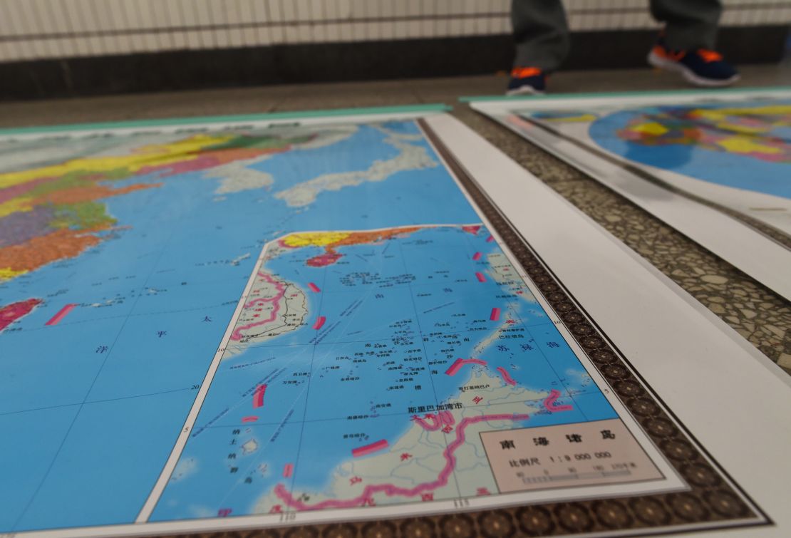 In this photo taken on June 15, 2016, a vendor stands behind a map of China including an insert with red dotted lines showing China's claimed territory in the South China Sea, in Beijing. 