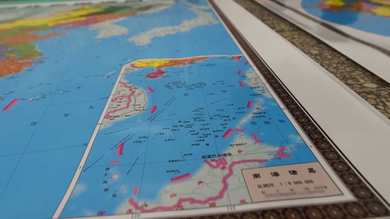 In this photo taken on June 15, 2016, a vendor stands behind a map of China including an insert with red dotted lines showing China's claimed territory in the South China Sea, in Beijing.