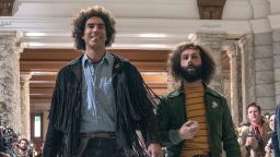 "Abbie Hoffman" (Sacha Baron Cohen) and "Jerry Rubin" (Jeremy Strong) walk down a courthouse hallway lined with reporters in "The Trial of the Chicago 7."