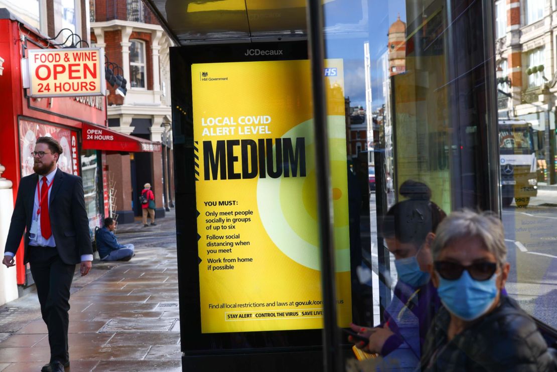 Commuters wearing masks at a bus stop near a poster showing that the local Covid alert level is Medium in London on Thursday, before it moves up to high on Saturday.