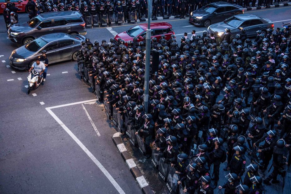 Motorists ride past riot police in Bangkok on October 15.